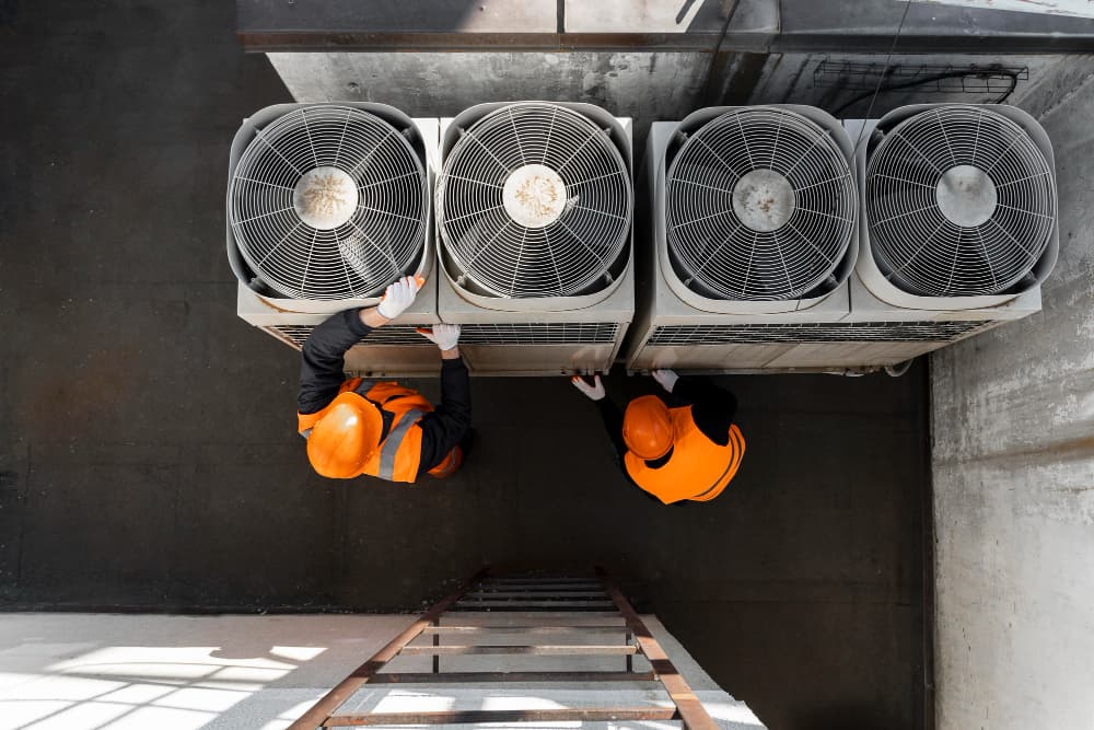 Technicians performing maintenance on rooftop air conditioning condensers, viewed from above
