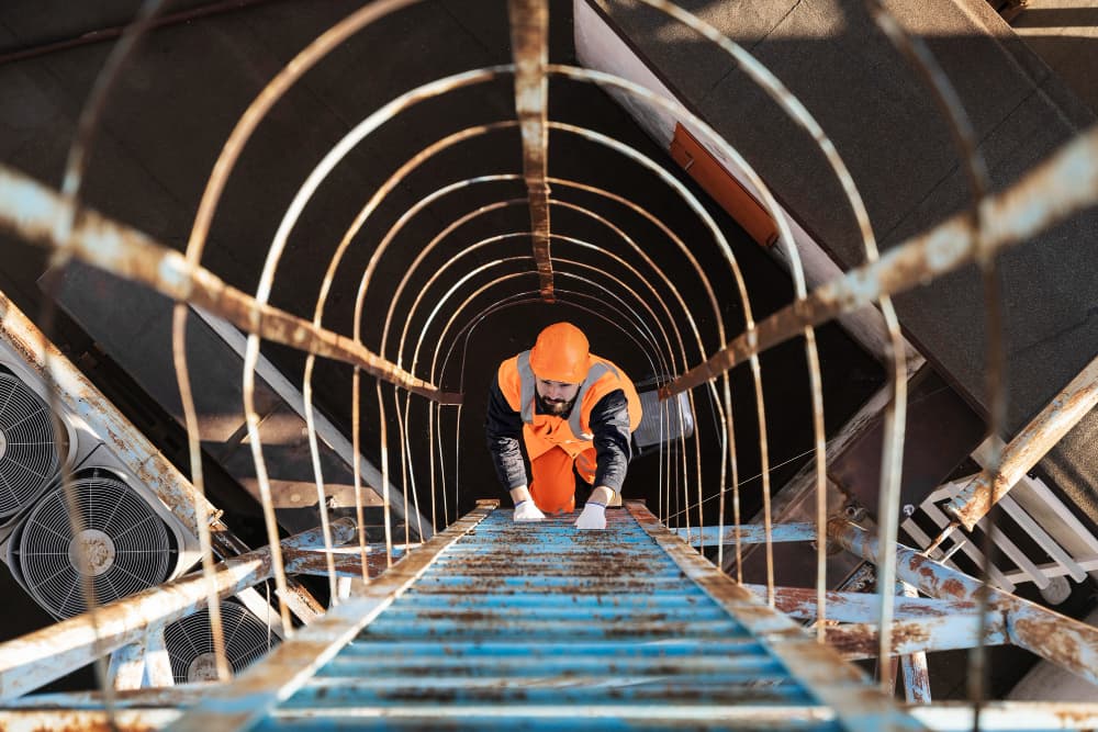 Technician climbing a caged ladder between commercial AC units