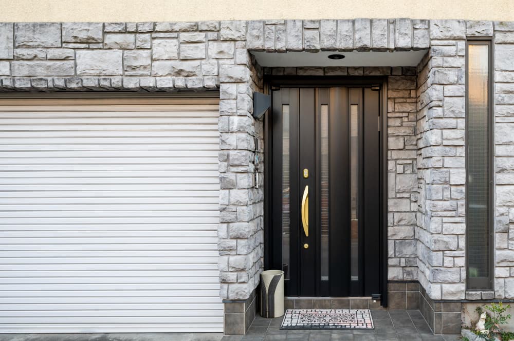 White garage door and black front entrance of a stone-faced home